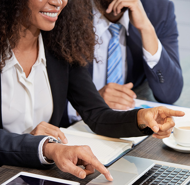 Faceless shot of coworking businesspeople surfing laptop while discussing project at table in office